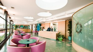 Eine Hotelhalle mit einer Rezeption, rosa Stühlen und Tischen.