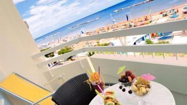 Ein Balkon mit gedecktem Tisch, mit Blick auf einen Strand mit Sonnenschirmen und Menschen.