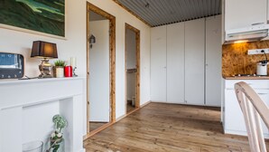 A modern kitchen with white cabinets, a wooden floor, and a dining area with a chair. - Blue House B&B (Seltjarnarnes)