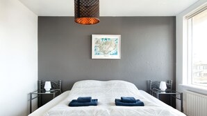 A modern hotel room with a large bed, two bedside tables with lamps, a framed map on the wall, and a view of the city through the window. - Blue House B&B (Seltjarnarnes)