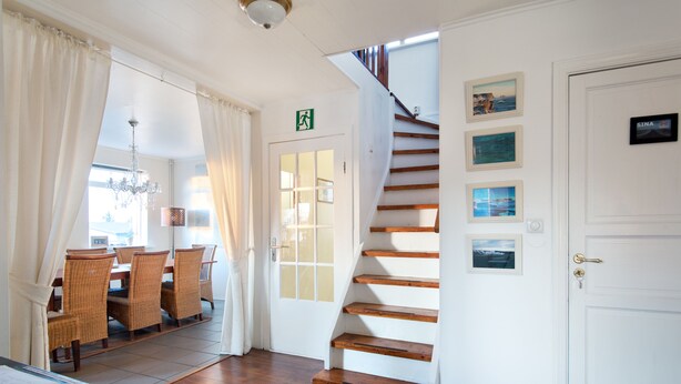 A hotel lobby with a staircase, a dining area with wicker furniture, and a white door with a sign. - Blue House B&B (Seltjarnarnes)