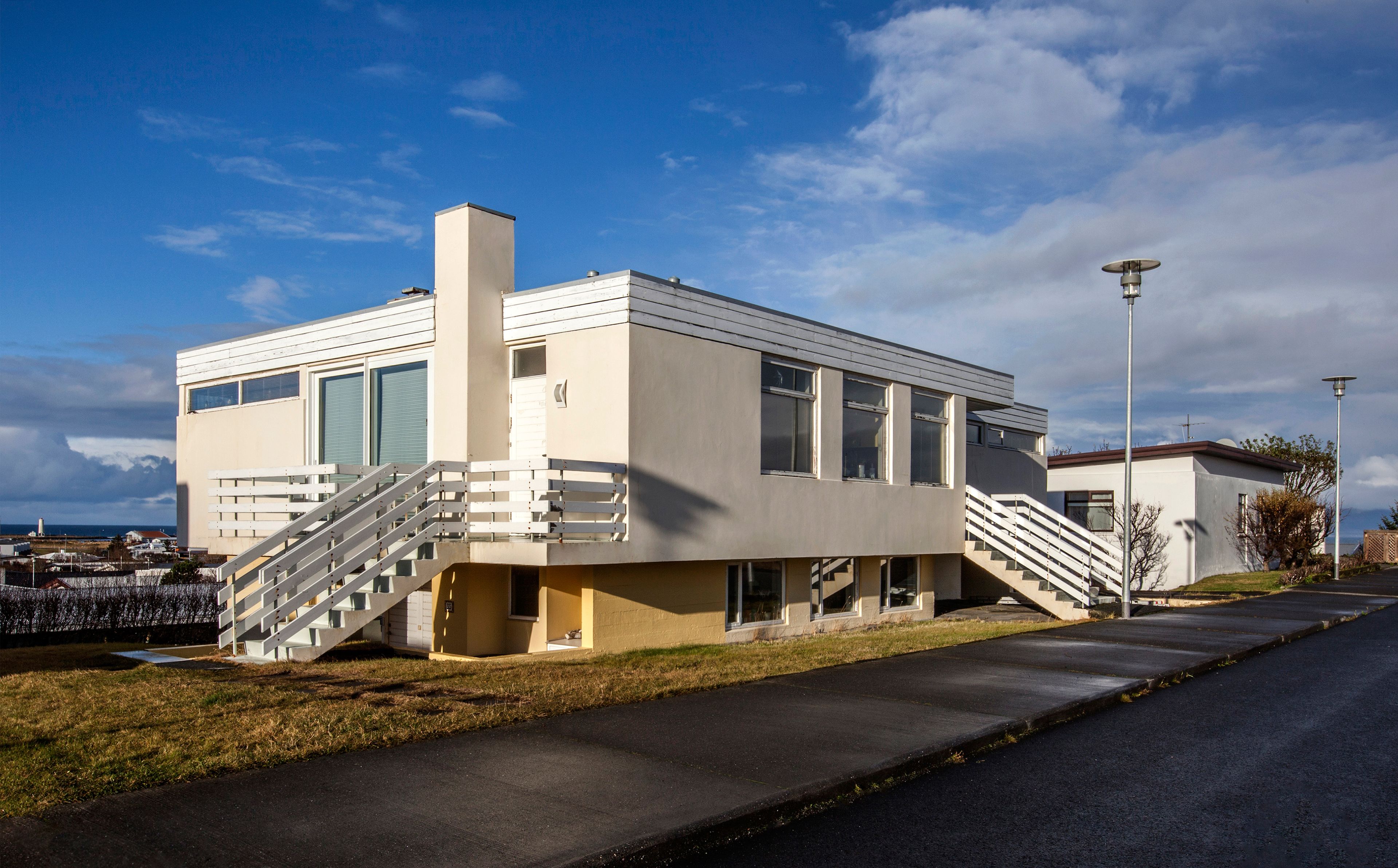 A modern two-story building with a flat roof, large windows, and a central chimney.