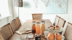 A dining table set with food and drinks, surrounded by wicker chairs, with a world map and chandelier in the background. - Blue House B&B (Seltjarnarnes)