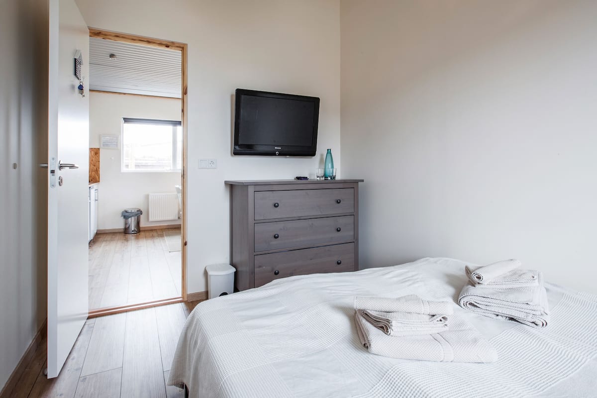 Un dormitorio con cama, cómoda, televisor y ventana.