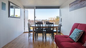 A dining area with a round table and chairs, a red sofa, and a view through a glass door. - Blue House B&B (Seltjarnarnes)