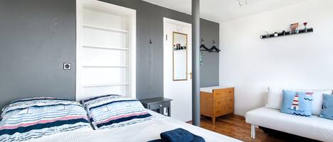 A bedroom with a bed, a dresser, a nightstand, a sofa, and a mirror.