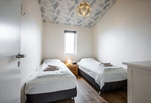 A bedroom with two beds, a window, a ceiling light fixture, and a bedside table with a lamp.