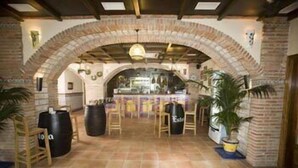 Un interior con un arco de ladrillo, sillas de madera, una zona de bar y plantas en macetas.