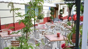 Un área de café al aire libre con mesas y sillas, plantas en macetas y un arreglo floral rojo.