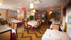 Comedor con varias mesas preparadas para el servicio, con piso de diseño en zigzag e iluminación colgante roja.