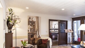 A hotel lobby with a red carpet, a brown leather armchair, a wooden cabinet with wine bottles, and a signboard. - Hotel Restaurant Ruppert (Walluf)