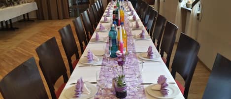 A long dining table set with chairs, a white tablecloth, and purple napkins.
