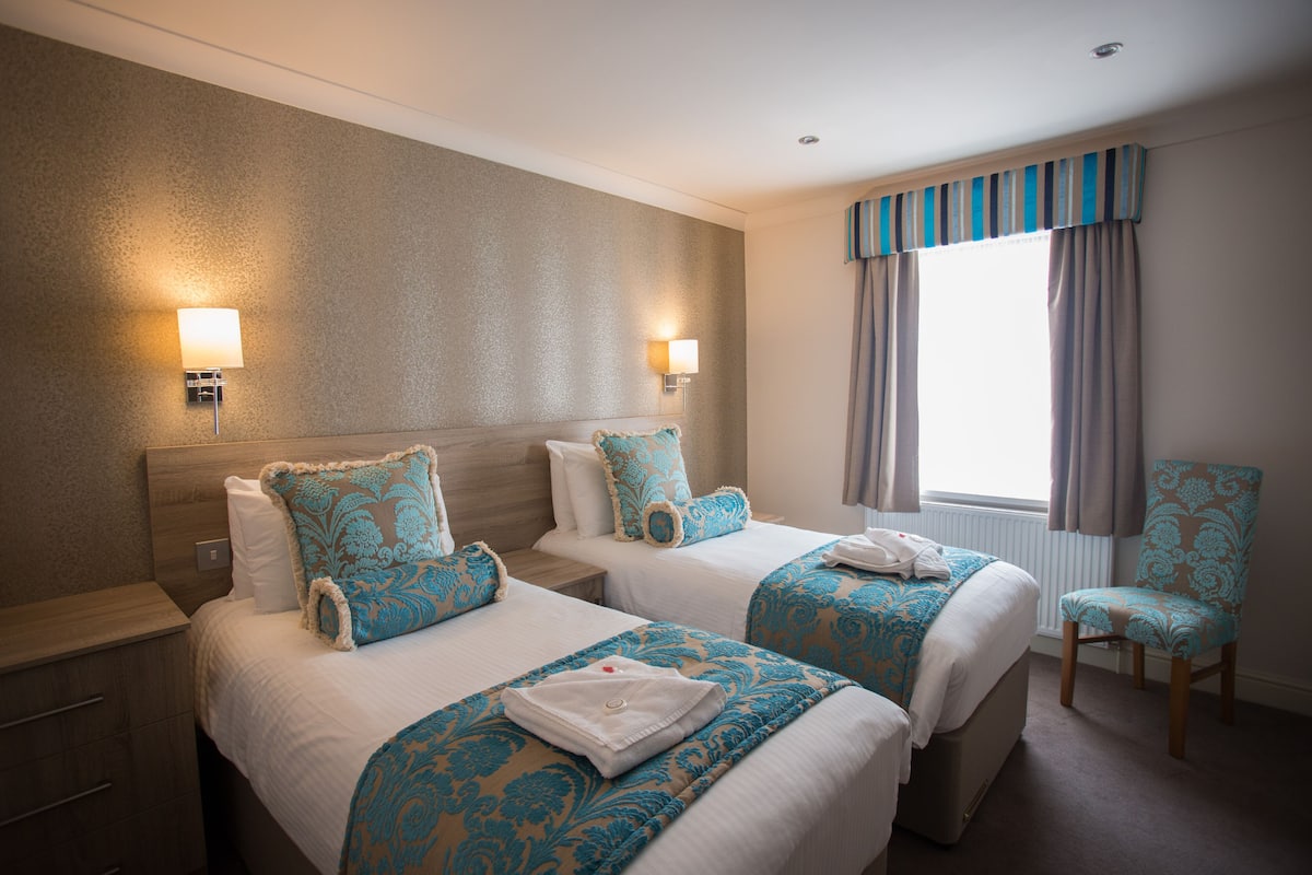 A hotel room with two beds, a chair, and a window with curtains.