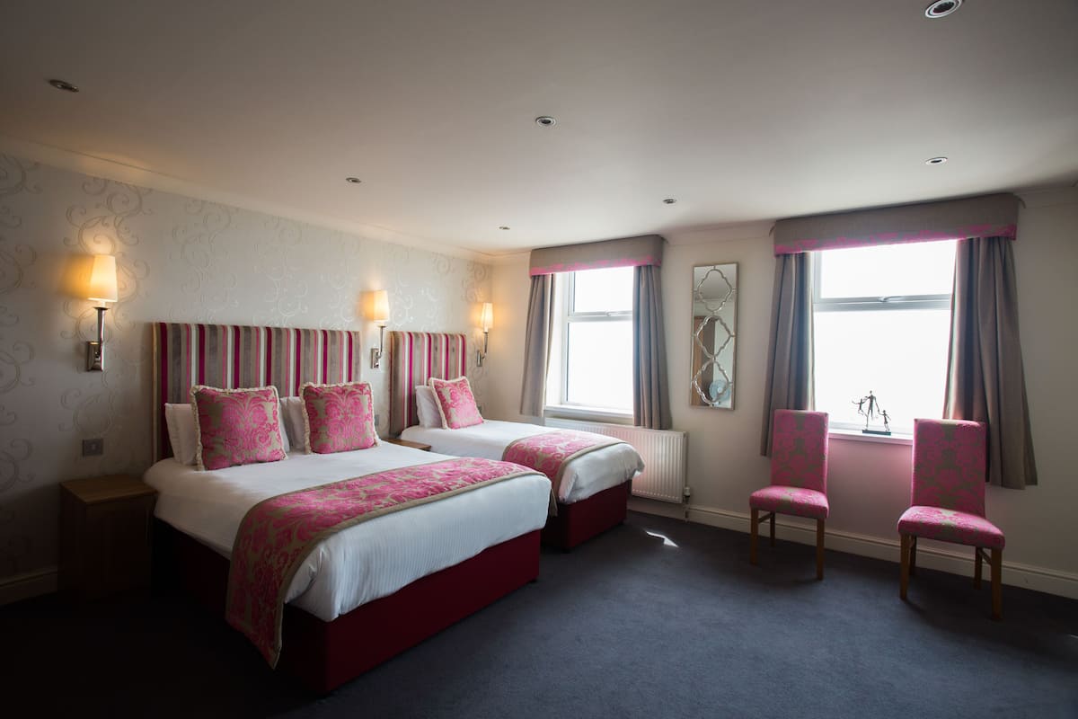A hotel room with two beds, a chair, and a view of the sea.
