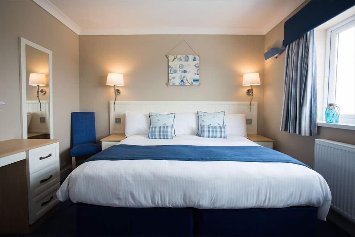A hotel room with a large bed, two bedside lamps, a chair, a dresser, and a window with curtains.