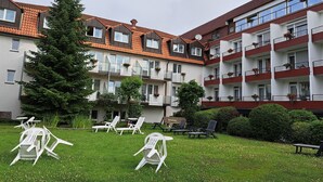 A multi-story residential building with balconies, a lawn with outdoor furniture, and a large evergreen tree.