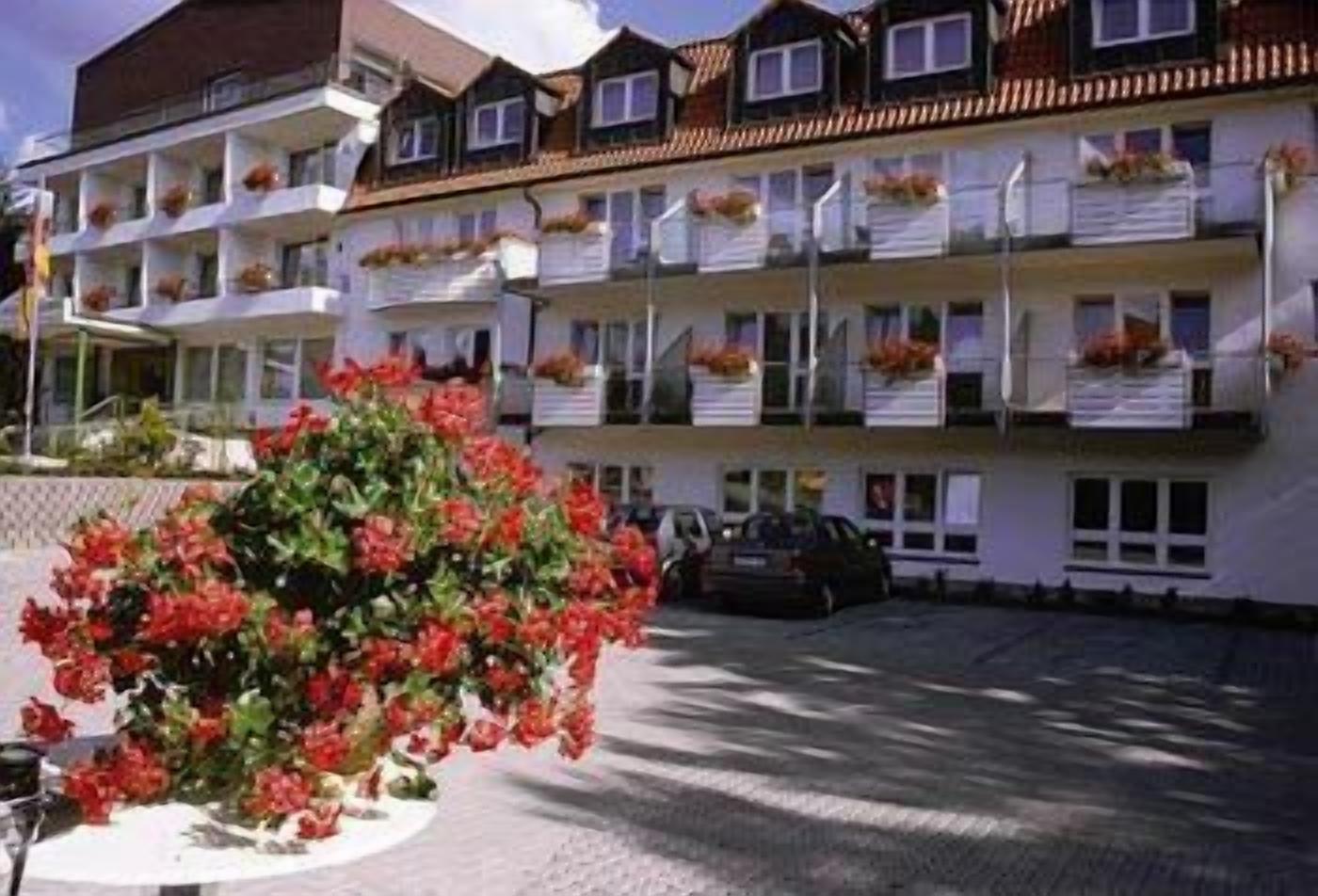 Un hôtel à plusieurs étages doté de balcons, d’un parking et d’un grand buisson au premier plan.