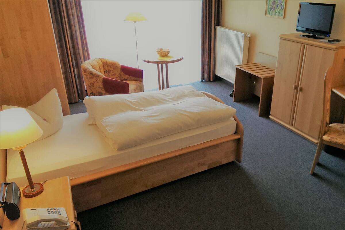 Una habitación de hotel con una cama, un escritorio con lámpara, una silla, una mesita con un cuenco, un televisor y un armario.