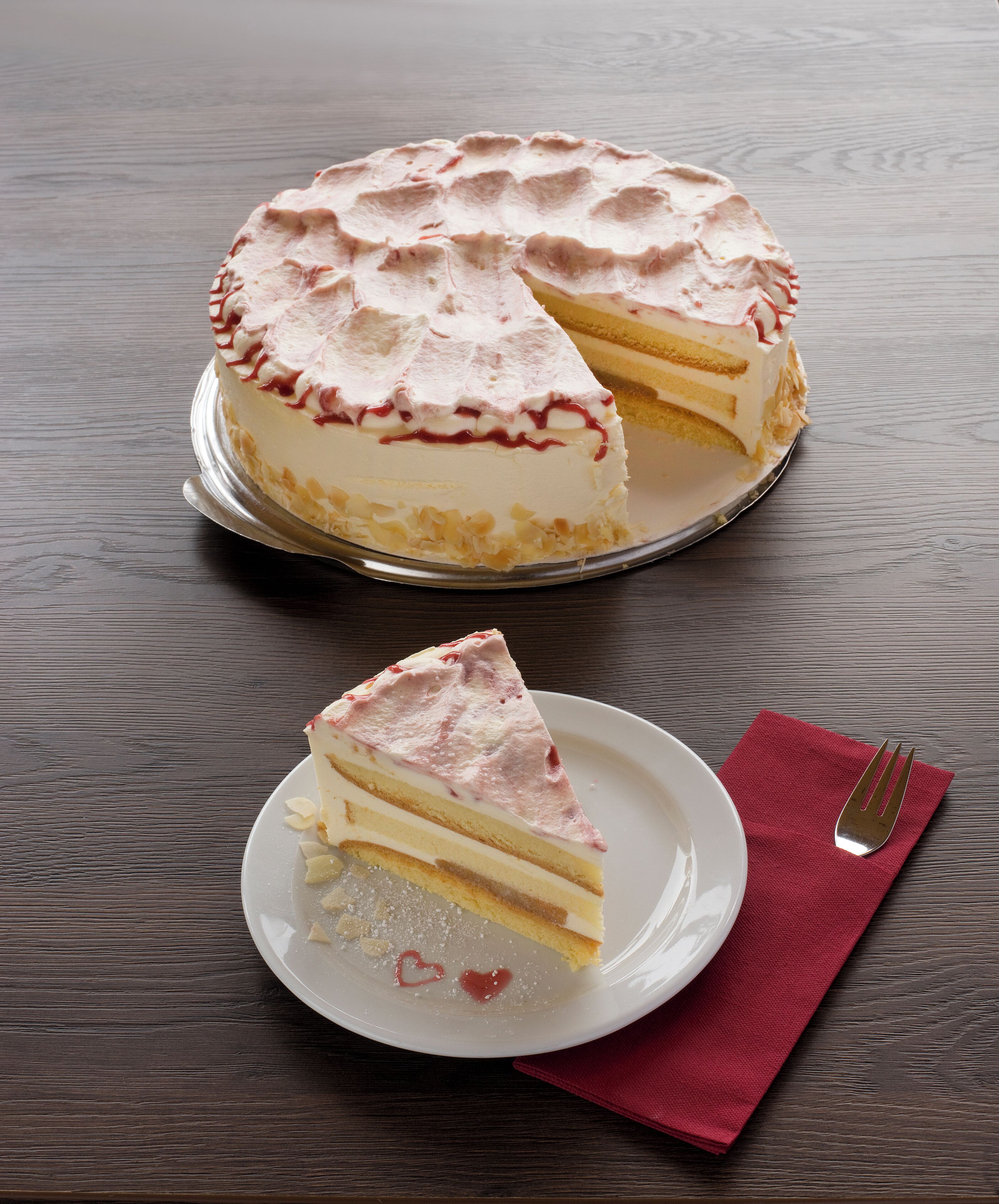 Una torta con una fetta rimossa, su un piatto con un tovagliolo rosso e una forchetta accanto.