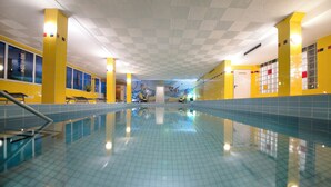 An indoor swimming pool with tiled walls and ceiling, yellow accents, and lounge chairs along the sides.