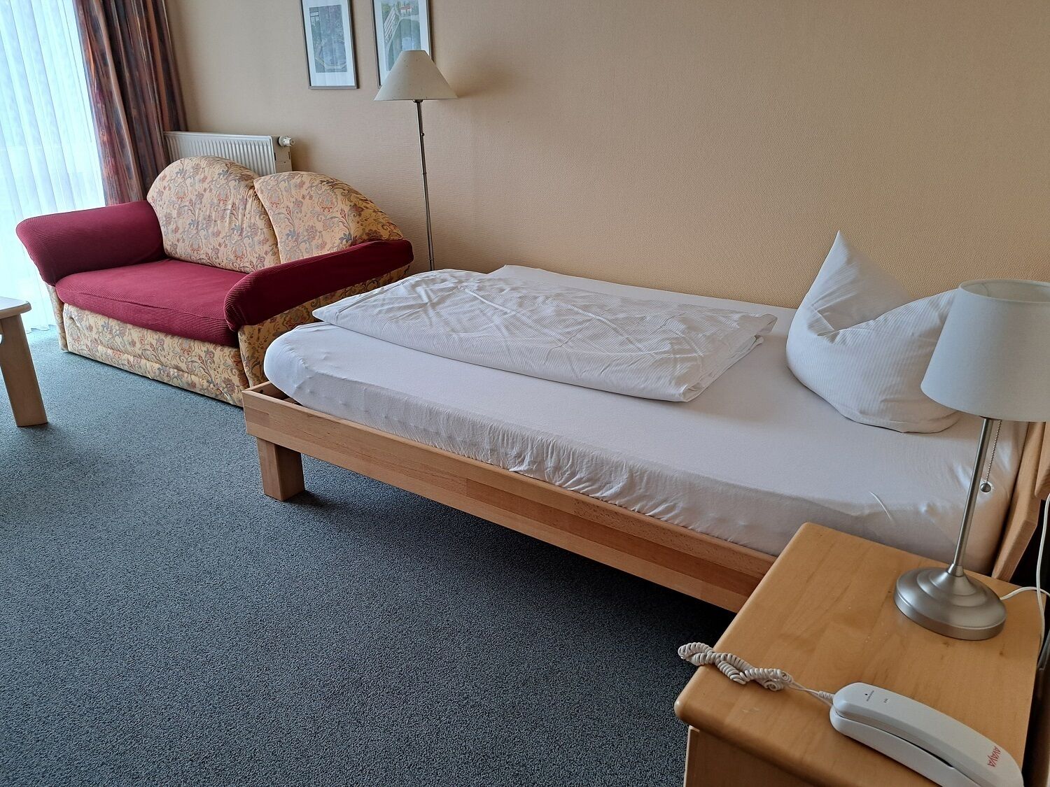 Une chambre d’hôtel avec un lit, une chaise, un bureau avec un téléphone et deux lampes.