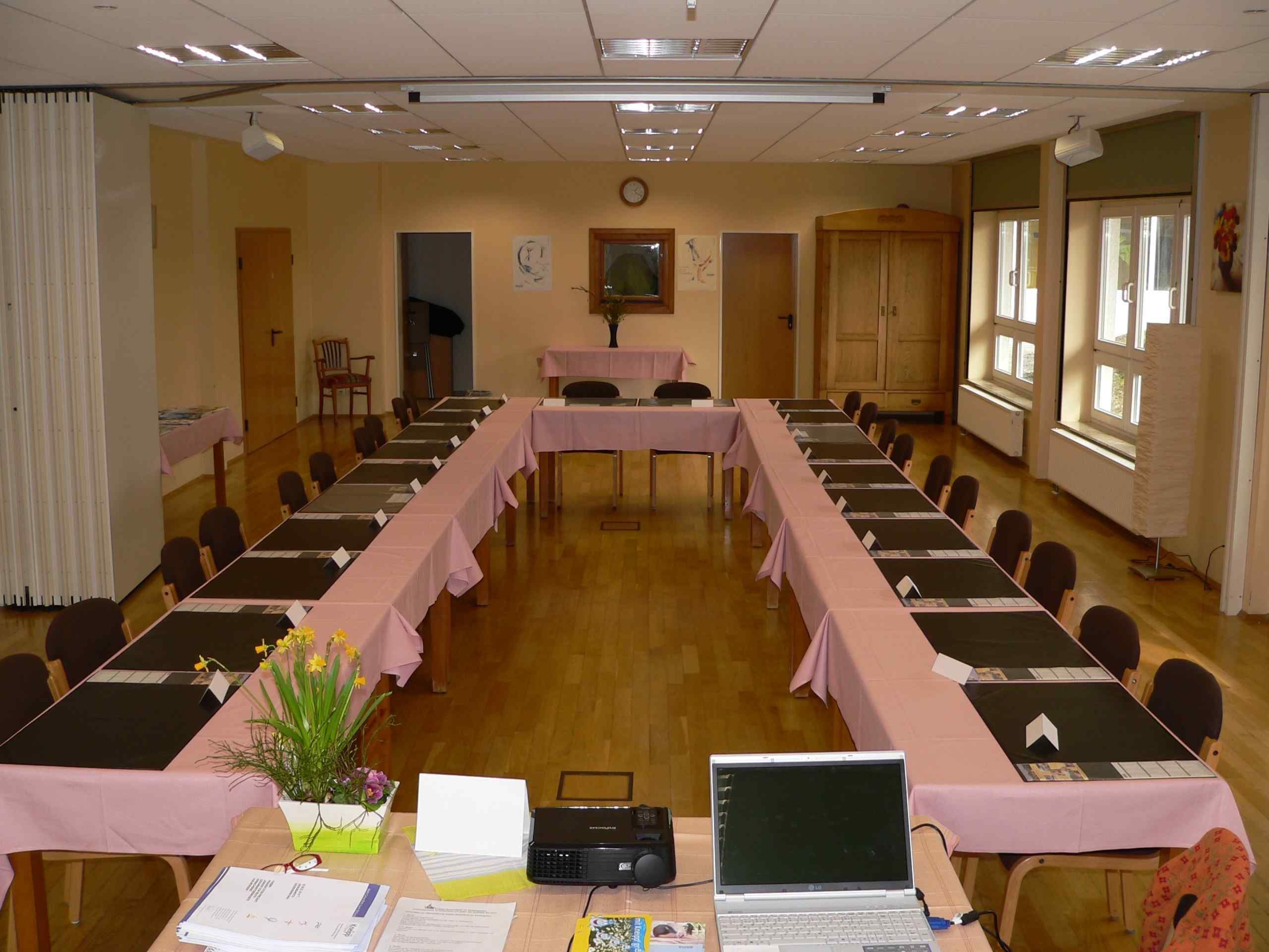Ein Konferenzraum mit langem Tisch, Stühlen, einer Uhr und einem Fenster.