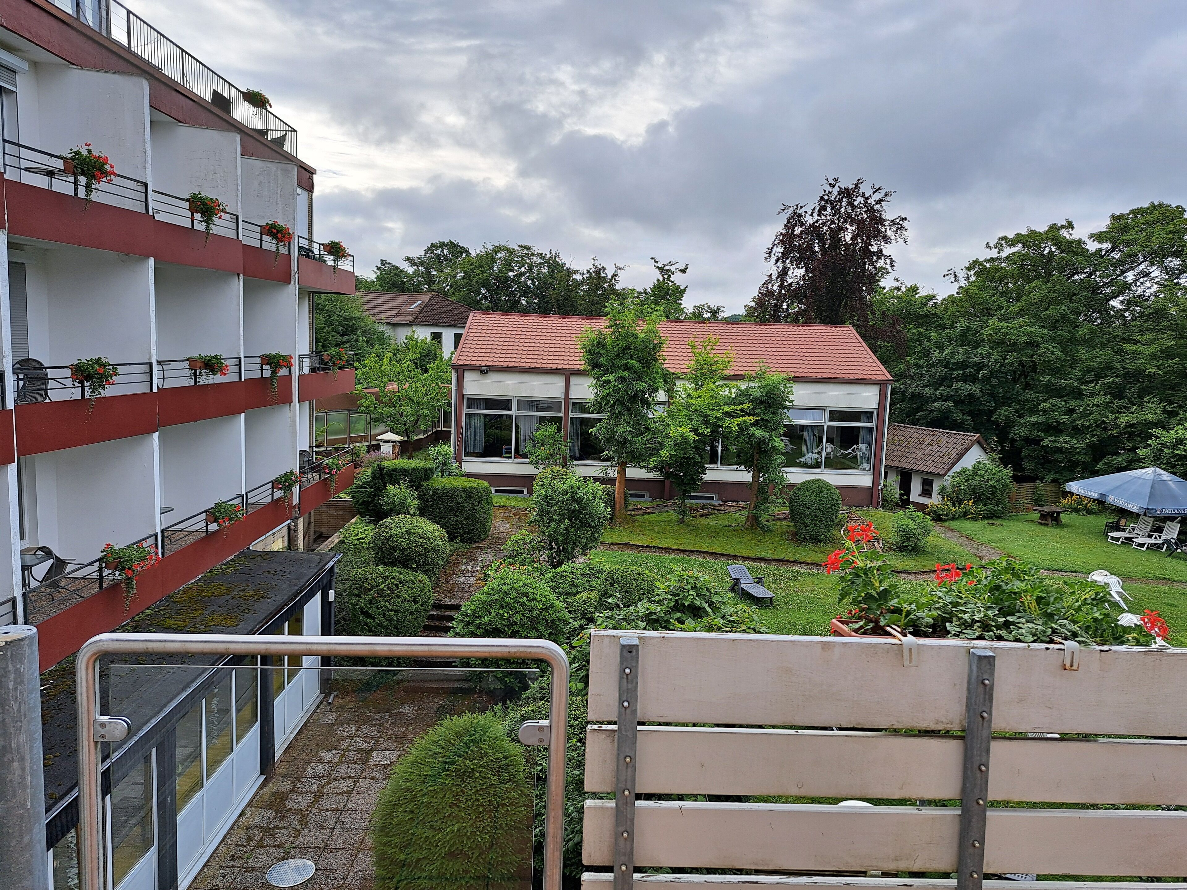 A residential building with multiple balconies, a garden with various plants, and a small house with a red roof.