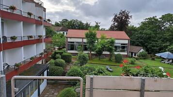 Ein Wohngebäude mit mehreren Balkonen, ein Garten mit verschiedenen Pflanzen und ein kleines Haus mit rotem Dach.