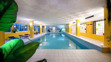 An indoor swimming pool with blue tiles, yellow walls, and a ceiling with a geometric pattern.