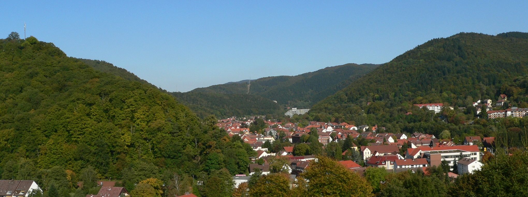 Un pueblo enclavado en un valle con casas de tejados rojos y colinas verdes y frondosas.