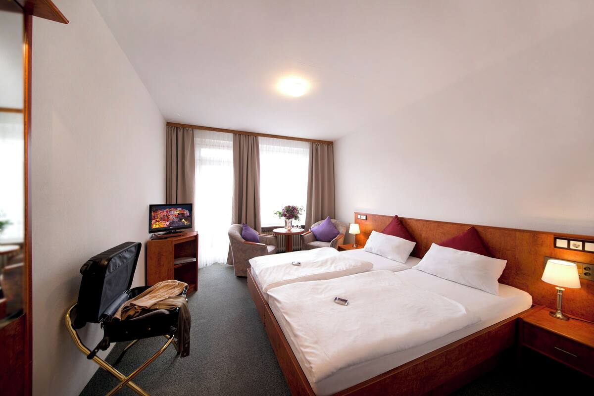 Habitación de hotel con dos camas, un escritorio con computadora, una silla y un televisor.
