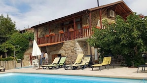 Um edifício de pedra com varanda, piscina e espreguiçadeiras.