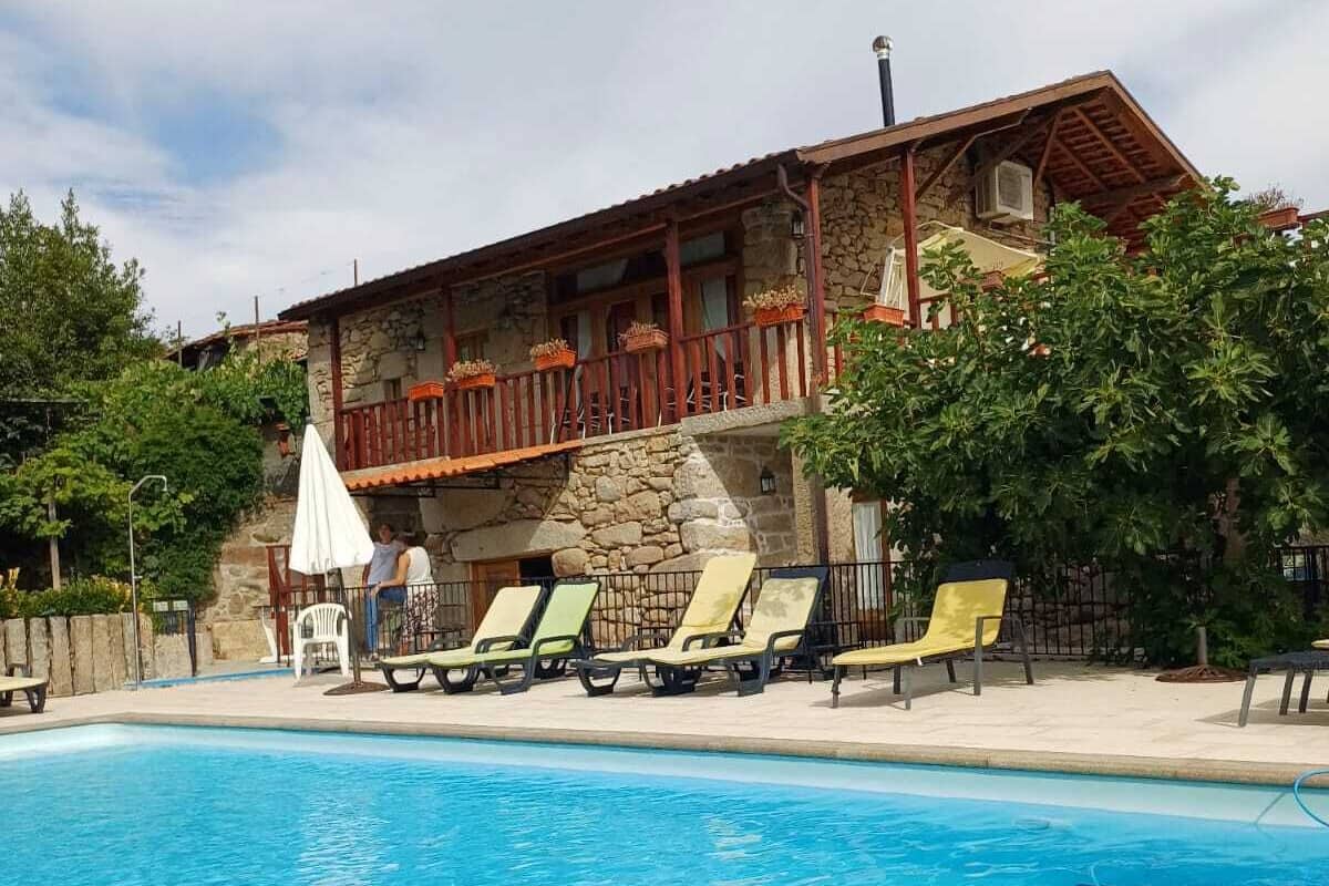 A stone building with a balcony, a swimming pool, and lounge chairs.