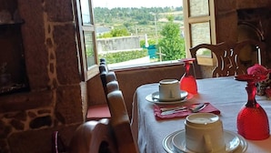 Uma área de refeições com uma mesa posta para dois, vista para o verde lá fora e paredes de pedra.