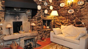 Um quarto acolhedor com lareira de pedra, um sofá branco e um tapete estampado.