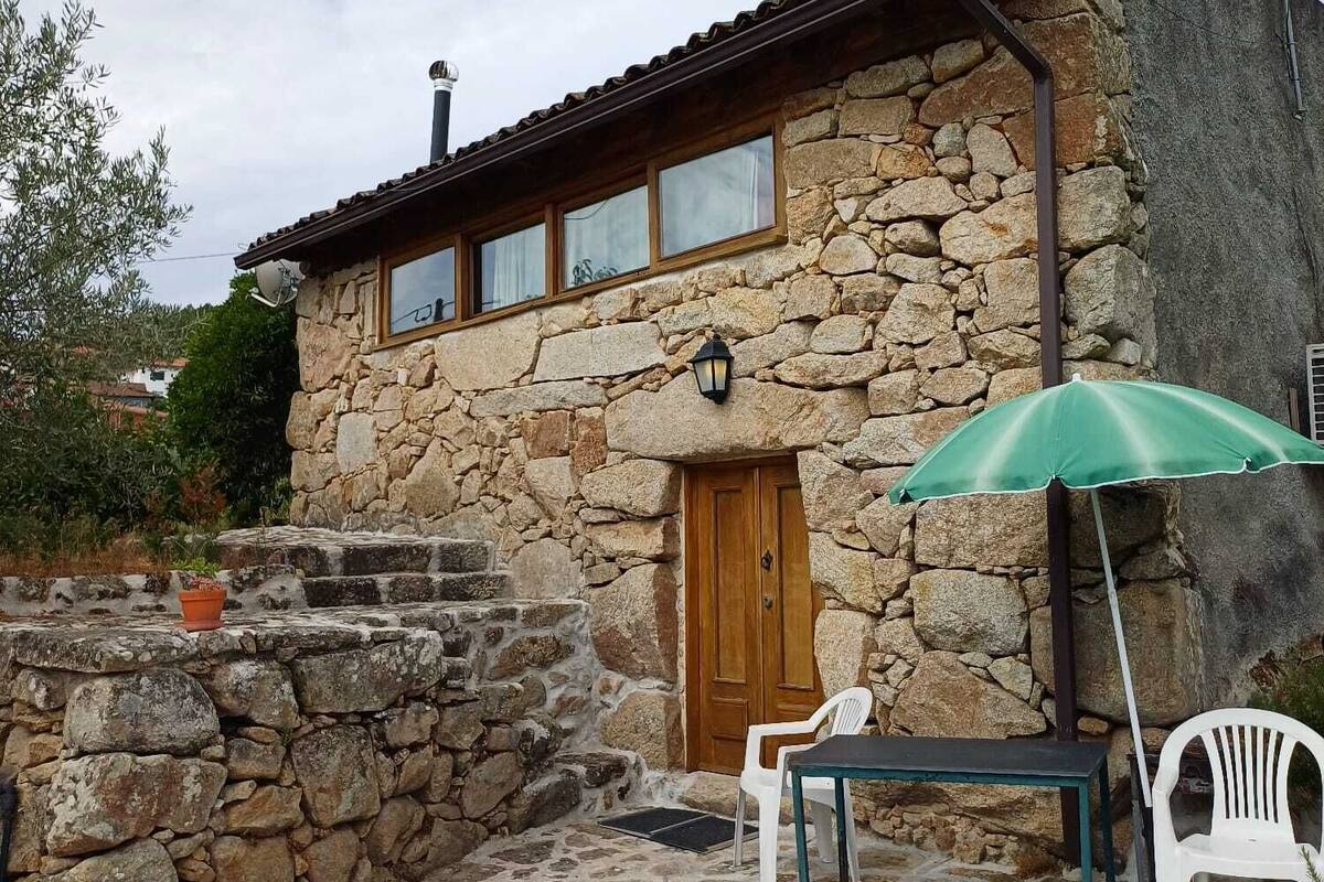 A stone building with a wooden door, a small porch with a bench, and a green umbrella.
