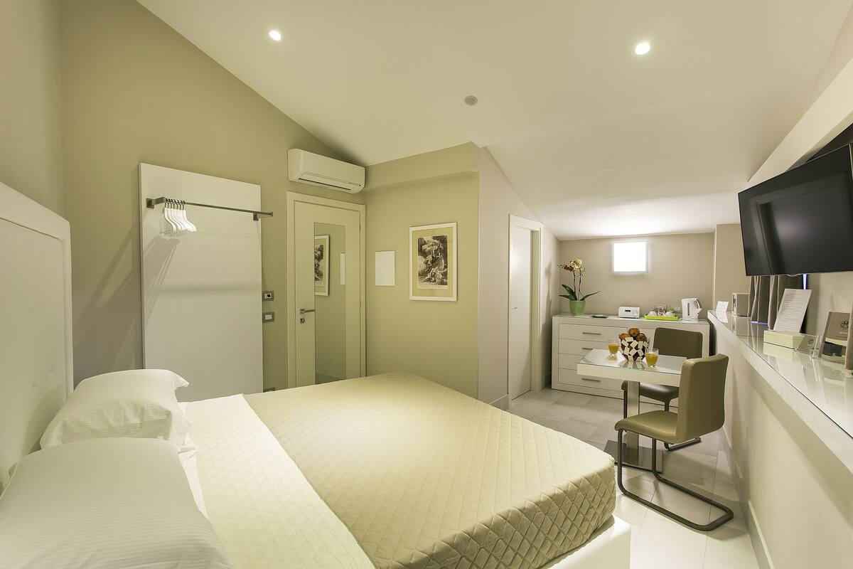 A hotel room with a bed, a desk with a chair, a television, and a small kitchenette.
