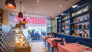 A restaurant interior with checkered tablecloths, blue and white patterned walls, and a display case with food items. - Magi House Relais (Sorrento)