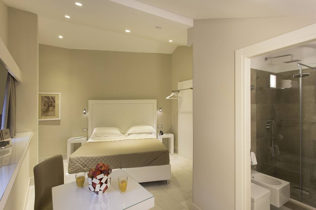 A modern hotel room with a bed, bedside table, and a glass-enclosed shower area.