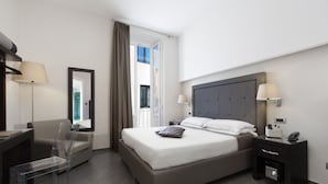 A modern hotel room with a large bed, a desk, a chair, and a nightstand with a lamp. - Magi House Relais (Sorrento)