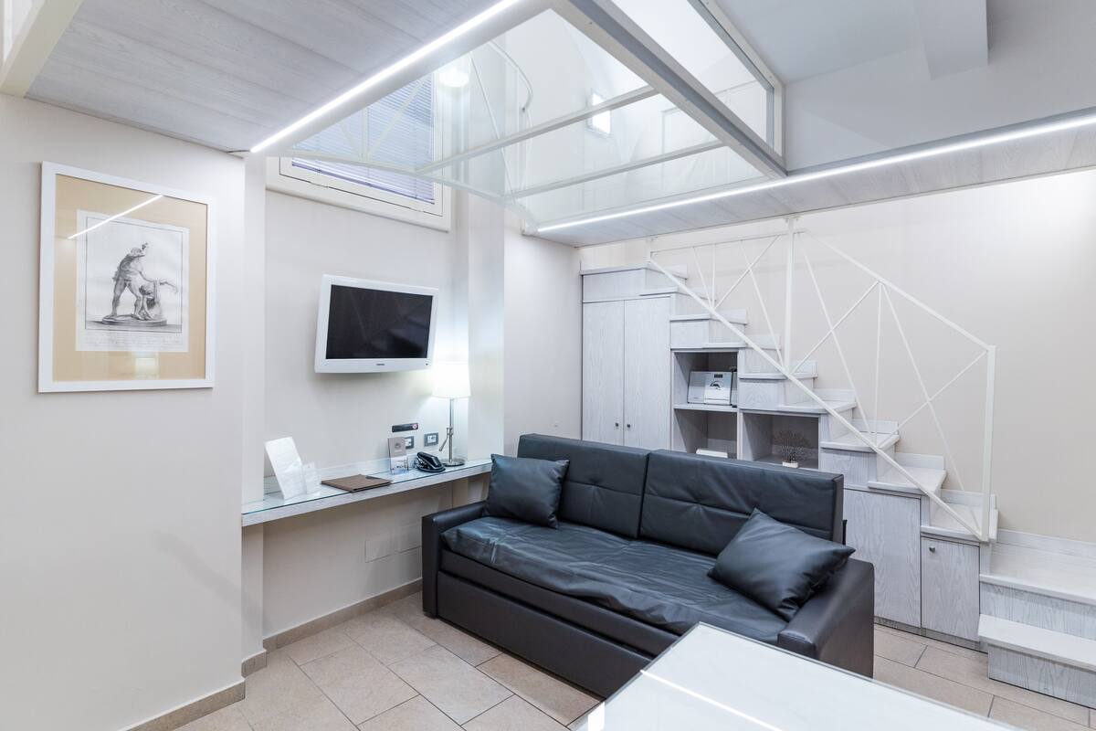 A modern interior with a sofa, a desk, a flat-screen TV, and a staircase.