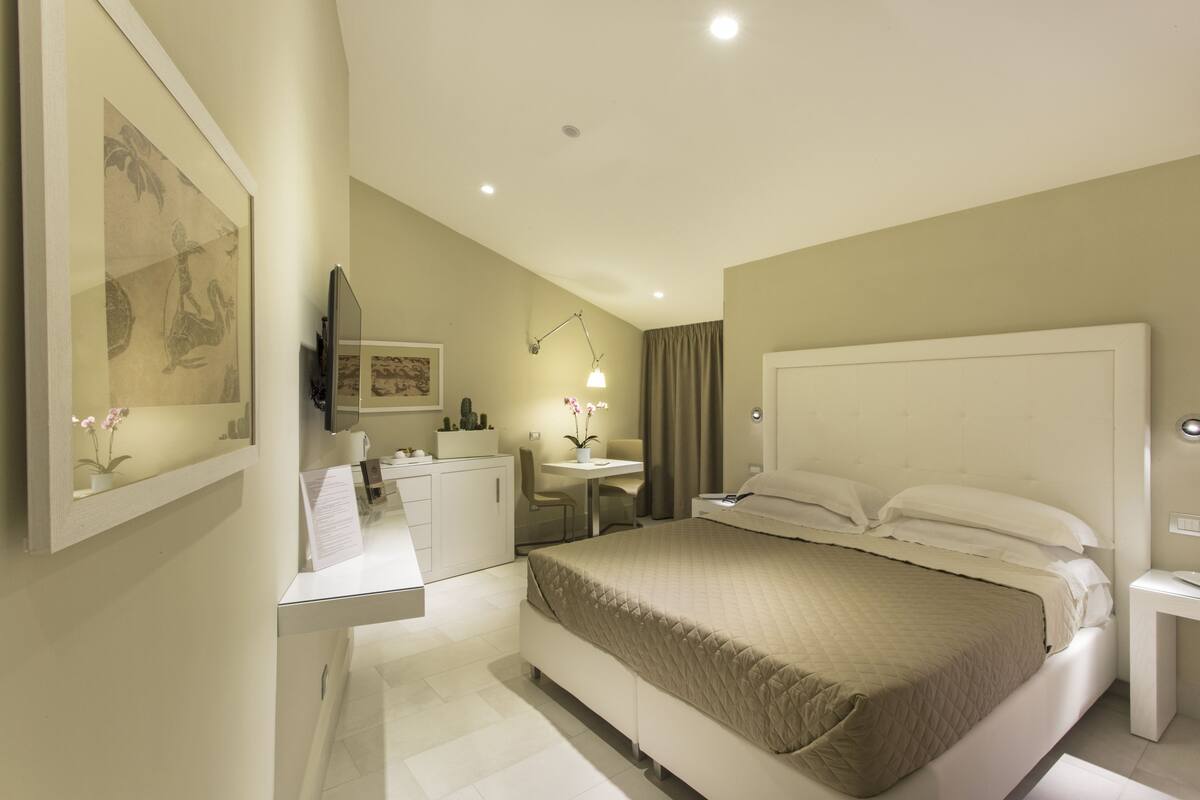 A hotel room with a large bed, a desk, a chair, a small table, and a mirror.