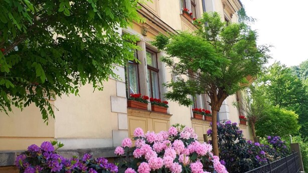 A building with classical architecture, featuring a balcony with red flowers and a wrought iron fence. - Gaestehaus Loschwitz (Dresden)