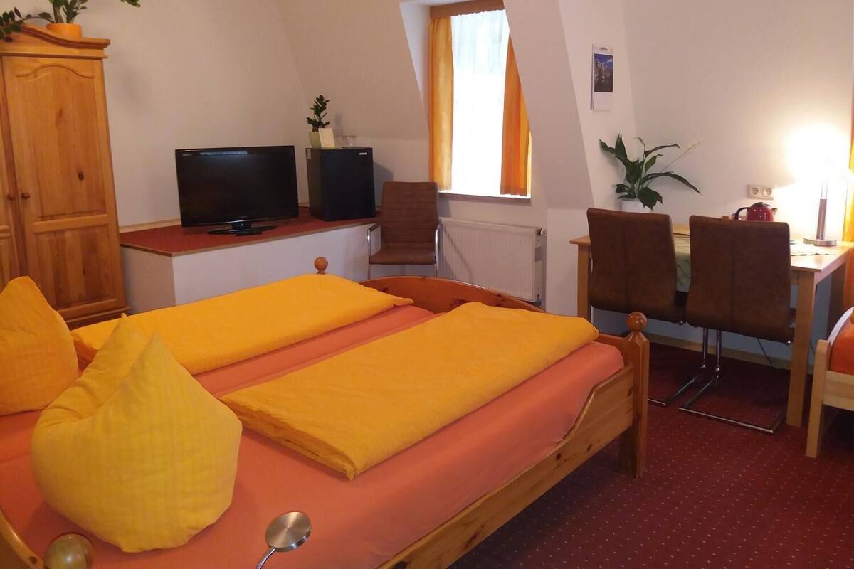 A room with a bed, a desk with a computer and speakers, a chair, and a window with curtains.