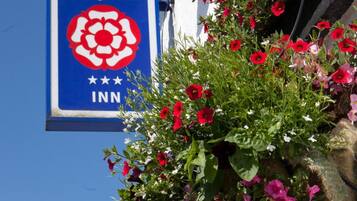 Um edifício com uma cesta suspensa cheia de flores vermelhas, cor-de-rosa e amarelas. Há uma placa com o logotipo de Enjoy England e o texto