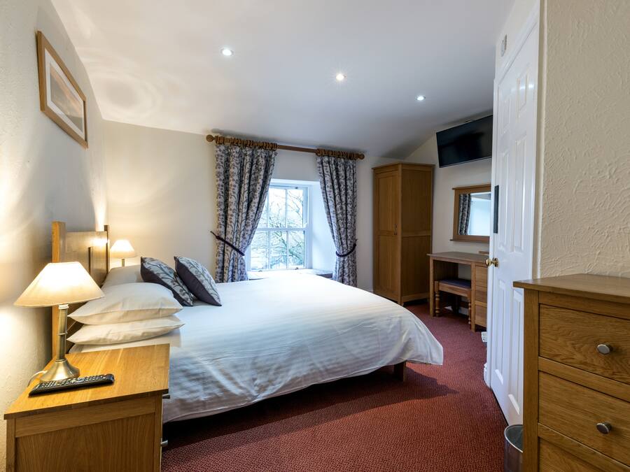 A neatly arranged bedroom with a bed, bedside lamp, and a desk with a chair.