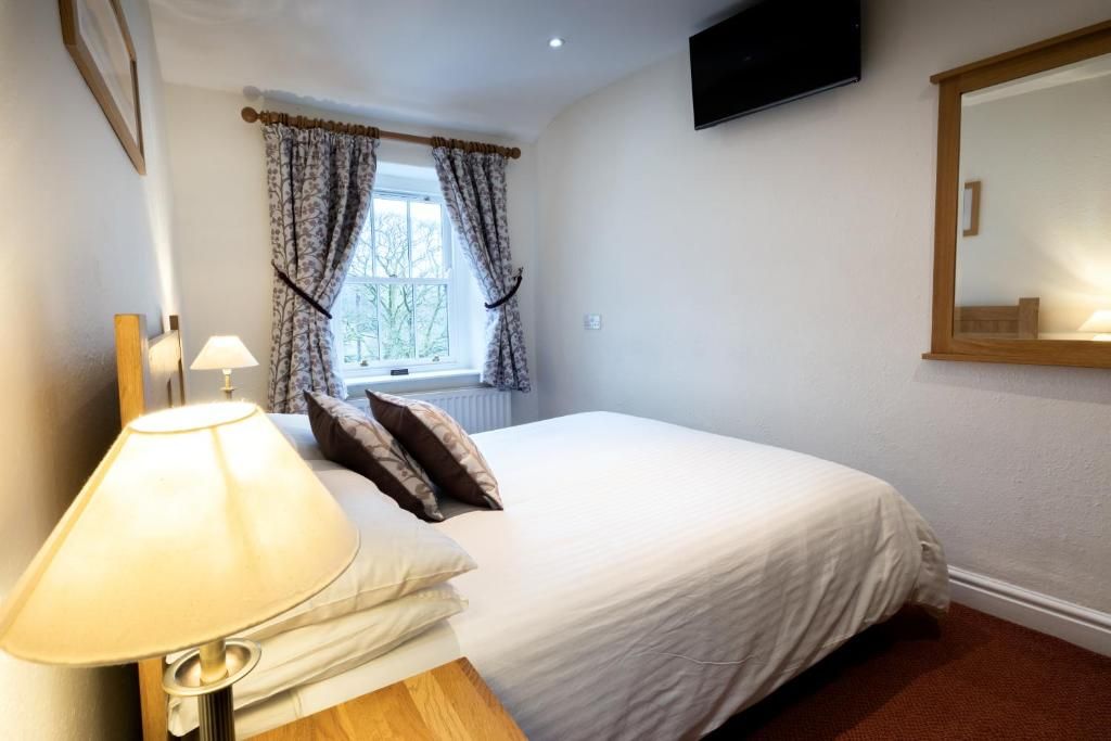Un dormitorio con cama, lámpara, ventana con cortinas, televisor en la pared y espejo.