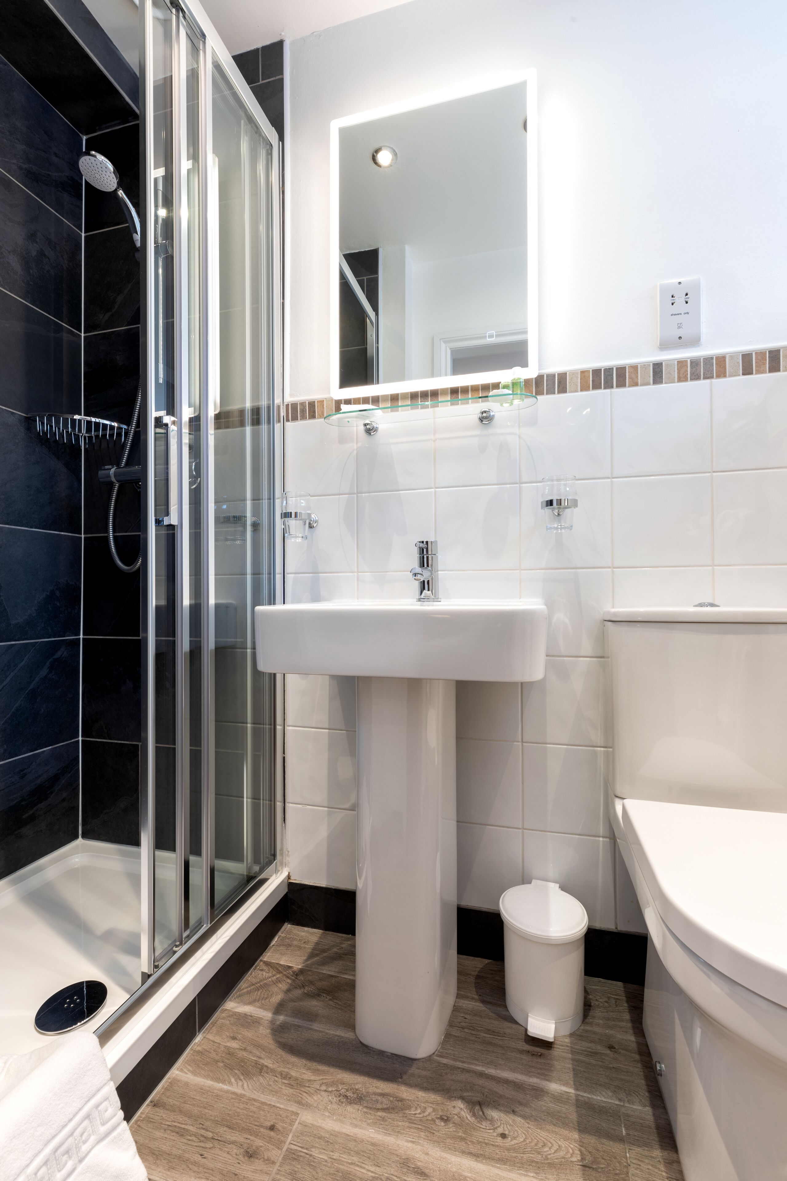 Un baño moderno con ducha de vidrio, lavamanos blanco y retrete.