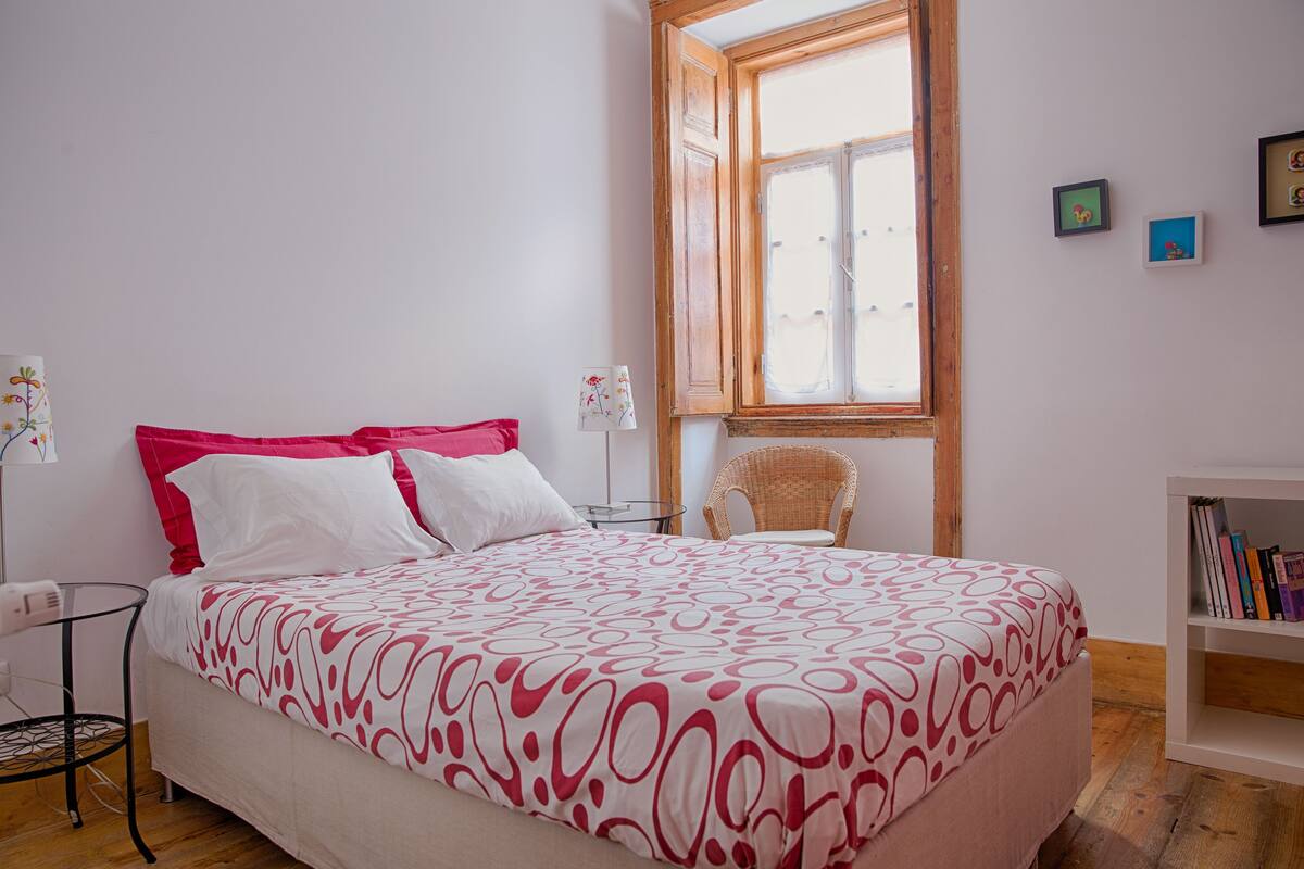 Un dormitorio con una cama, una silla, una mesita y una estantería.