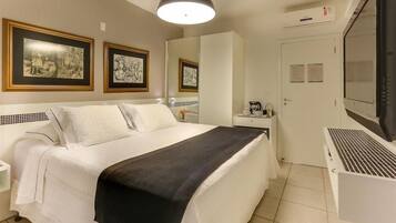 Una habitación de hotel con cama, escritorio, silla, televisor y cuadros en la pared.